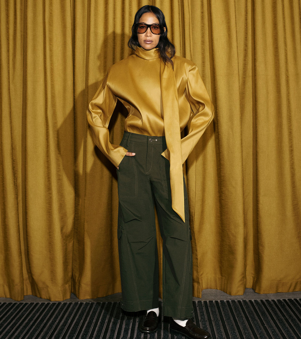 Woman wearing dark green wide-leg pants with a golden high-neck blouse and black loafers.