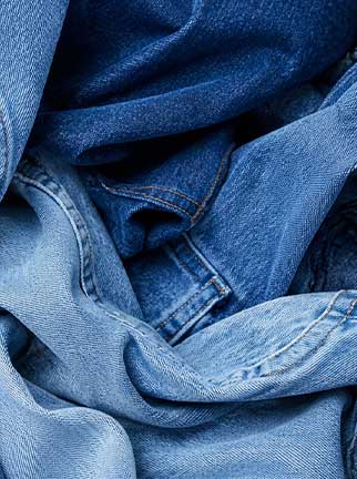 Close-up of layered light and dark blue denim fabrics, showcasing different washes, textures, and authentic stitching details.