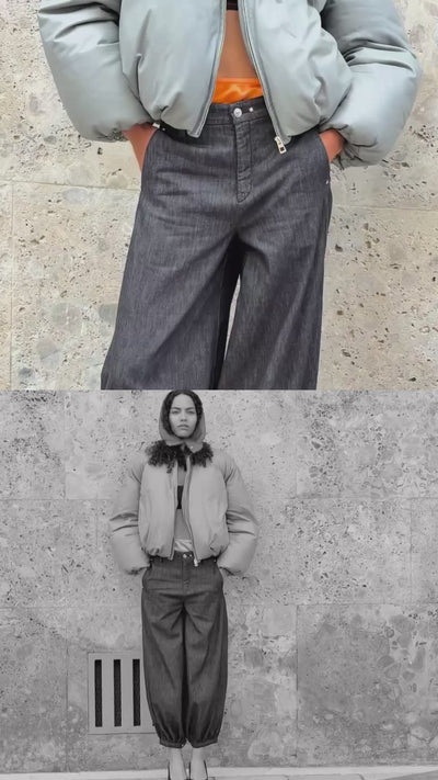 Woman wearing a light grey puffer jacket and dark denim barrel jeans. The video showcases the modern silhouette and fit of the jeans from both full-body and close-up perspectives against a stone wall background.
